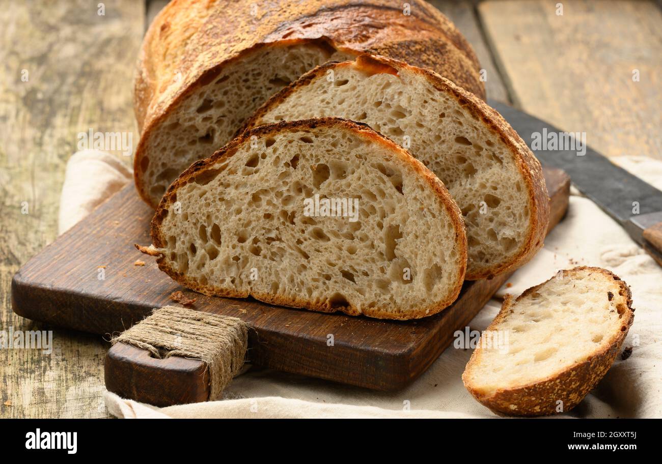 pane tondeggiante cotto a tavola di grano bianco su tavola di legno, pane tagliato a pezzi, primo piano Foto Stock
