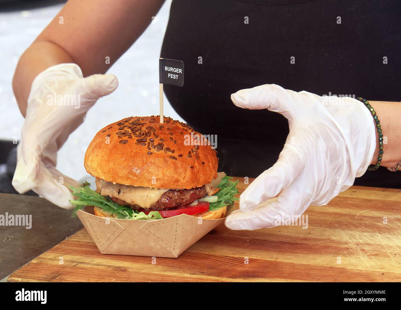 Uno chef prepara un hamburger per un cliente. Una donna che indossa guanti protettivi bianchi raccoglie una scatola di hamburger a portata di mano. Foto Stock