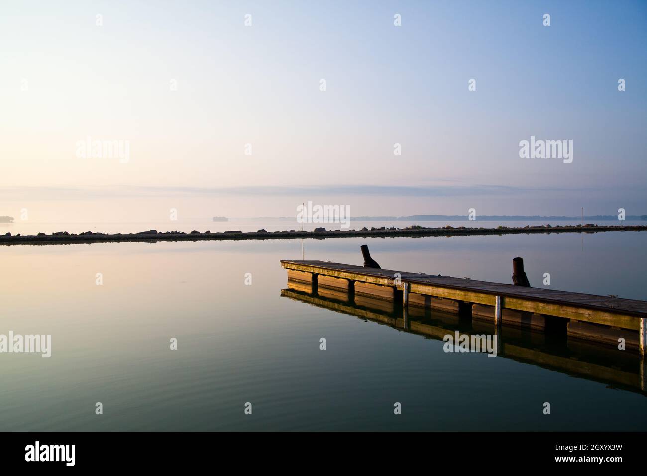 Lungo molo di legno si estende in un lago tranquillo in una giornata limpida Foto Stock