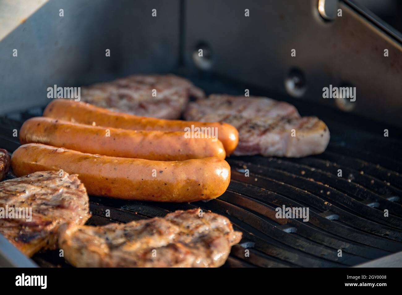 Grigliare salsicce tedesche e bistecche Juicy Sizzle on Flaming and Smoking Grill. Concetto di profumo alimentare. Foto Stock