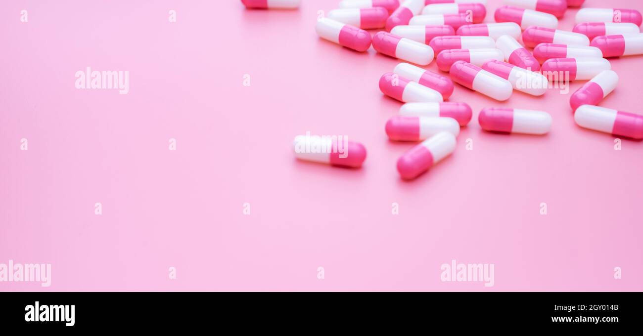 Capsule di antibiotico rosa-bianco su sfondo rosa. Resistenza agli antibiotici. Capsule pillole sparse su sfondo rosa. Uso di farmaci in ospita Foto Stock