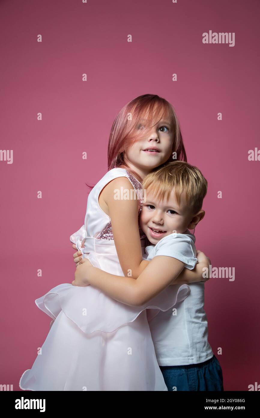 Caucasico fratello e sorella, abbracciando la fotocamera su sfondo rosa studio girato. Legami familiari, amicizia, concetto di infanzia felice. Foto Stock
