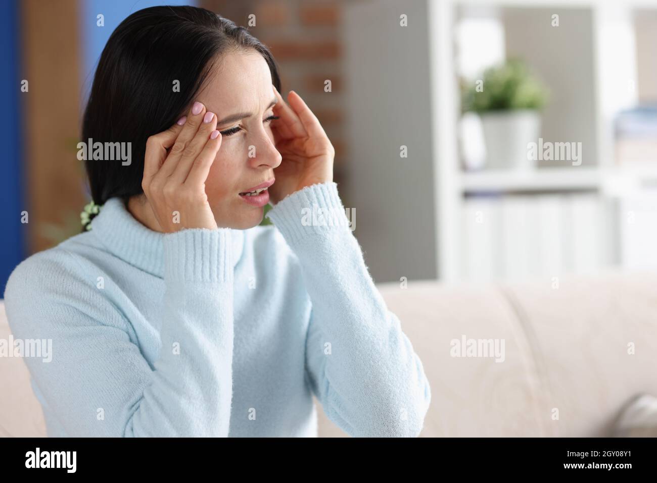 Donna con mal di testa e fotofobia guarda fuori finestra Foto Stock