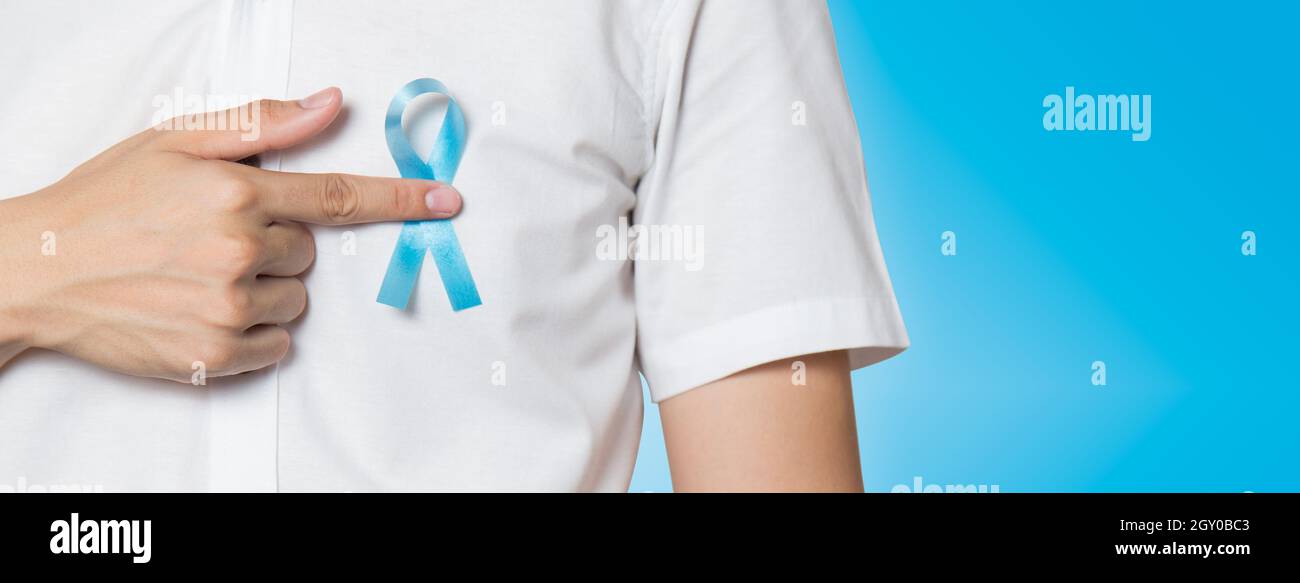 Concetto di salute degli uomini - primo piano della mano maschile che indica il nastro blu chiaro per il cancro della prostata al petto sinistro su sfondo blu. Banner con copia Foto Stock