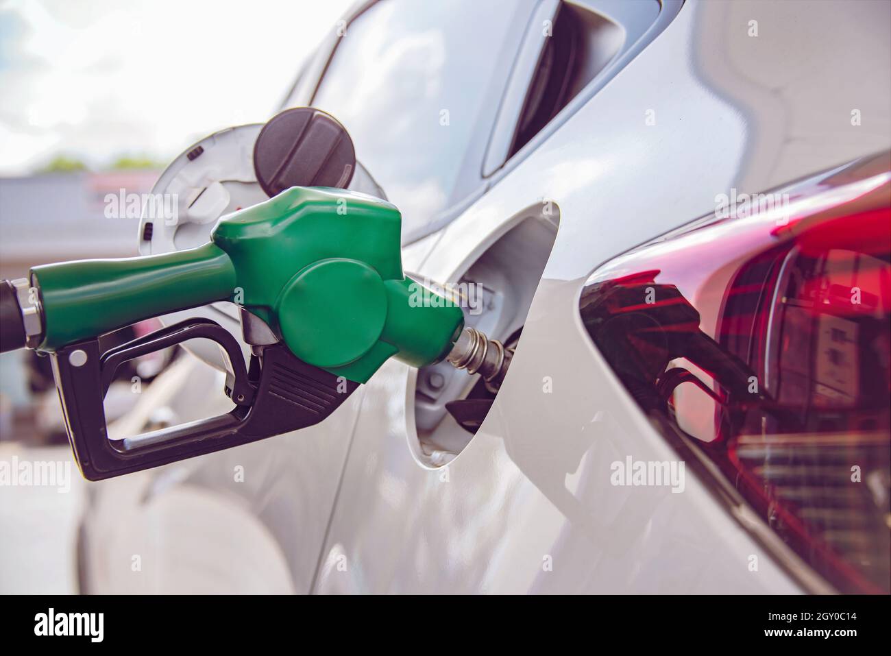 Impugnatura verde pompare l'ugello carburante benzina per il rifornimento. Impianto di rifornimento dei veicoli presso la stazione di servizio. Auto bianca al distributore di benzina che è riempito di carburante. Tran Foto Stock