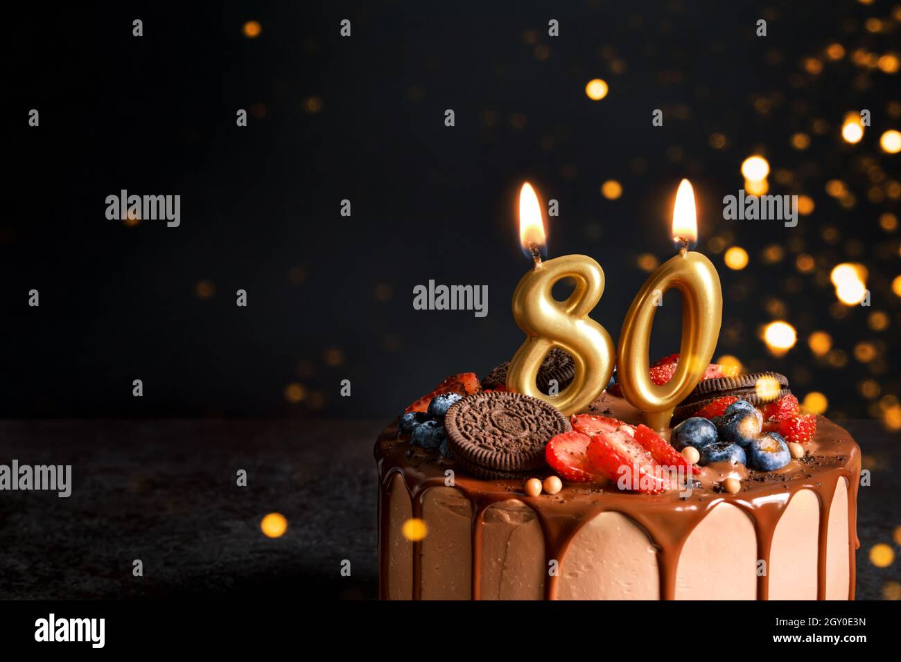 Torta di compleanno al cioccolato con frutti di bosco, biscotti e numero ottanta candele dorate su sfondo nero, spazio copia Foto Stock
