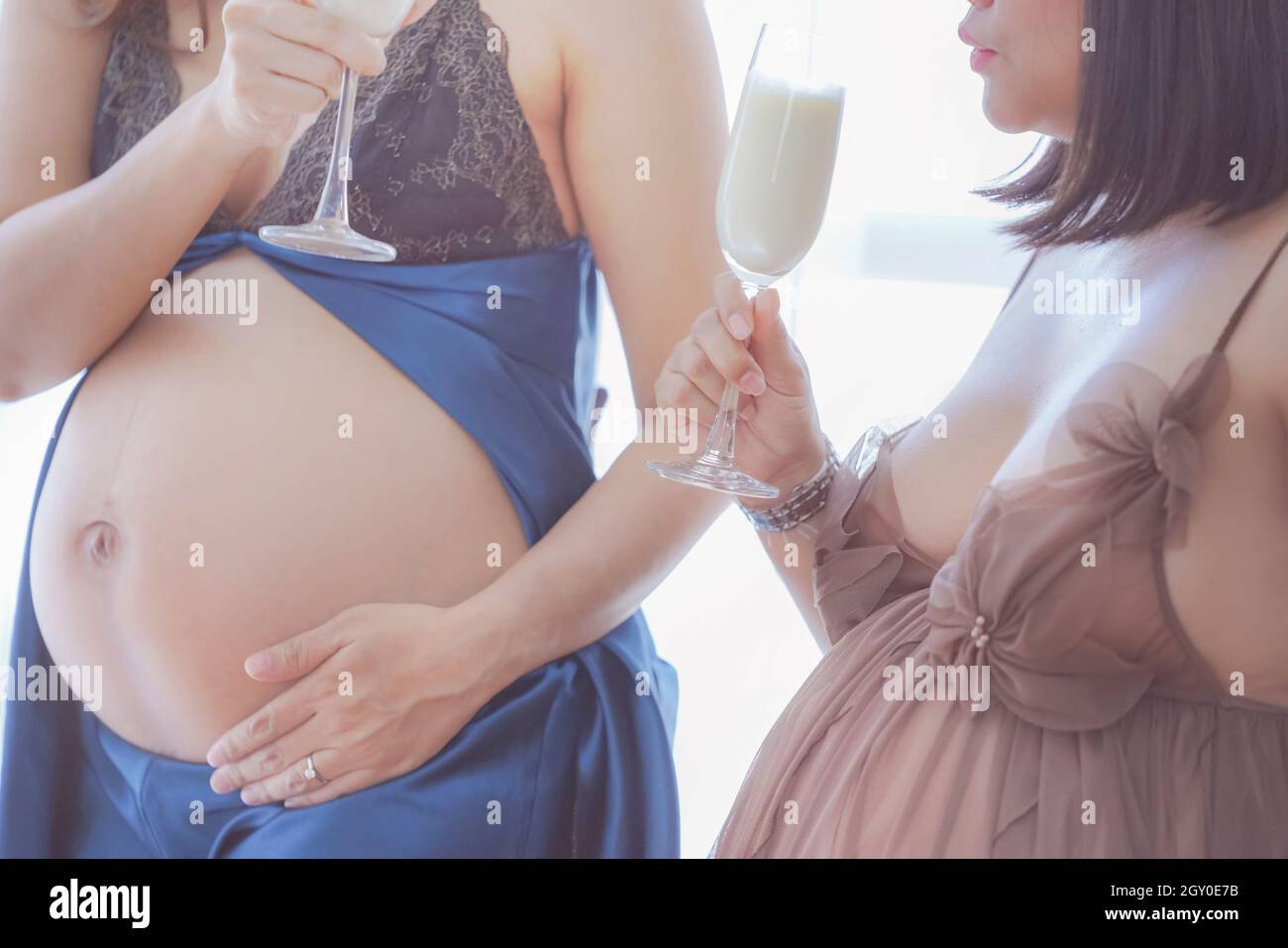Due giovani donne incinte che hanno latte fresco in vino o champagne festeggiato con la migliore amica per sempre. Primo piano Home ritratto di gravidanza giovane mumm Foto Stock