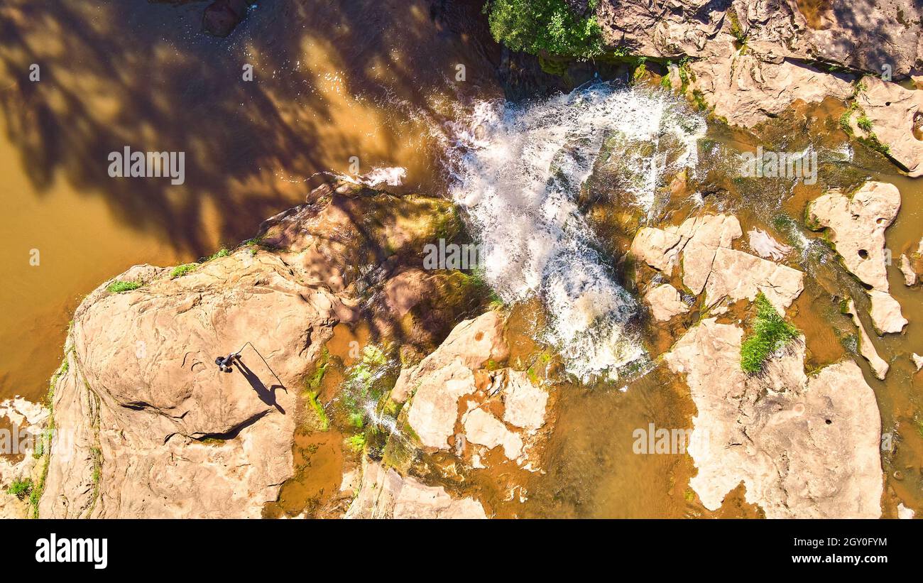 Guardando dritto verso il basso il fiume marrone con grande cascata e hiker casting ombra di figura Foto Stock