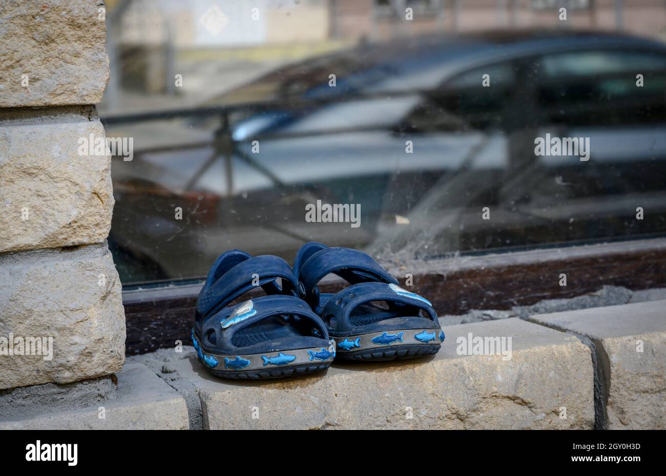 Pantofole per bambini sul davanzale di una casa in mattoni con il riflesso di un'auto nel vetro. Povertà, perdita, lusso Foto Stock