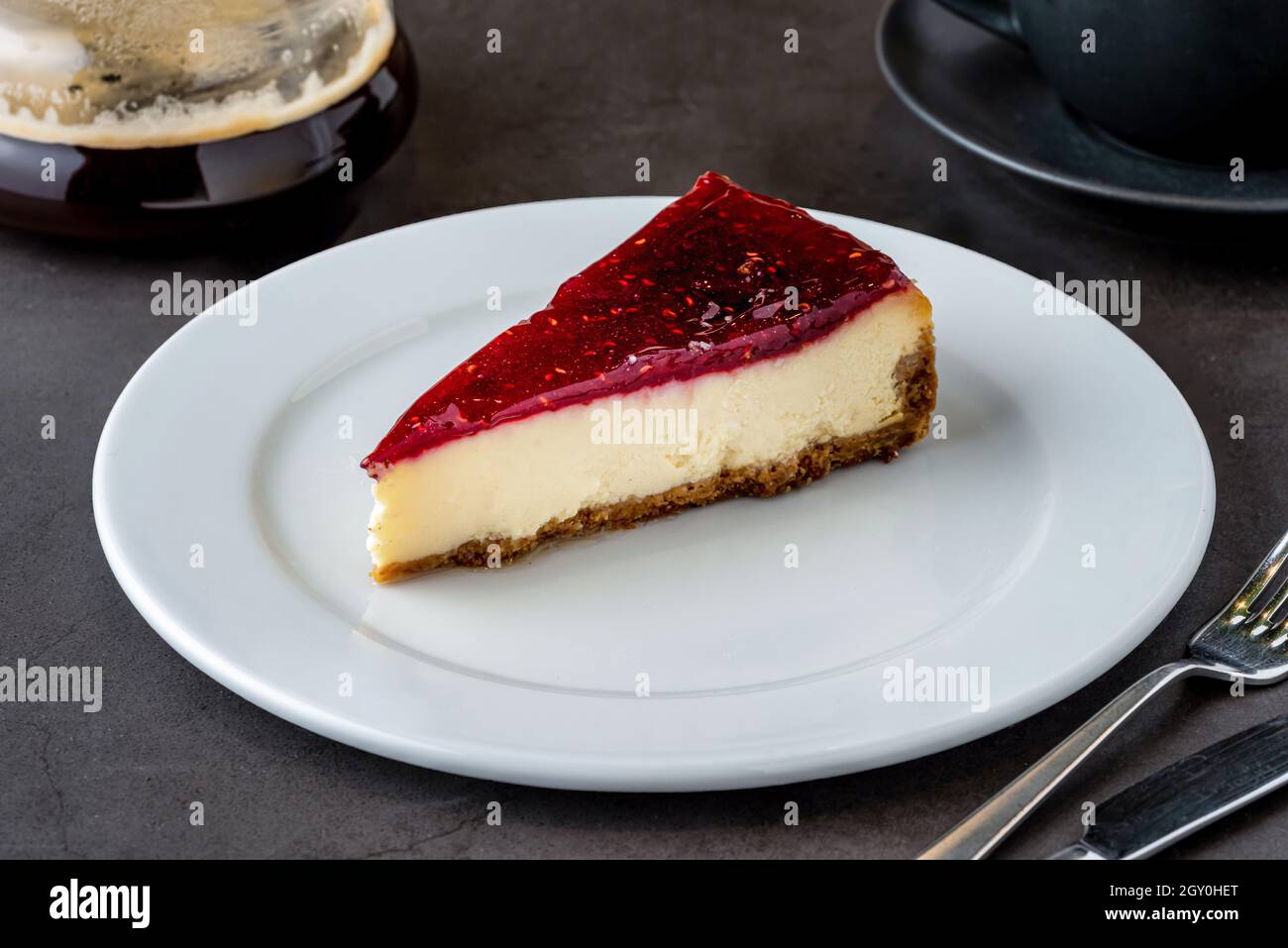 Cheesecake al lampone con caffè da caffè su tavola in pietra nera Foto Stock
