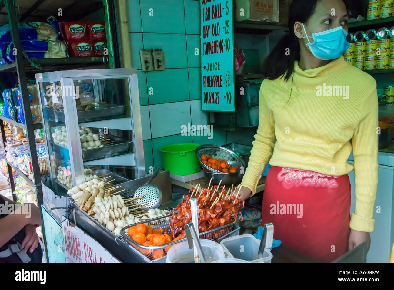 Venditore di strada femminile che vende palle di pesce fritte, spiedini di un giorno vecchi pulcini e altri fast food. Baguio città, Filippine. Foto Stock
