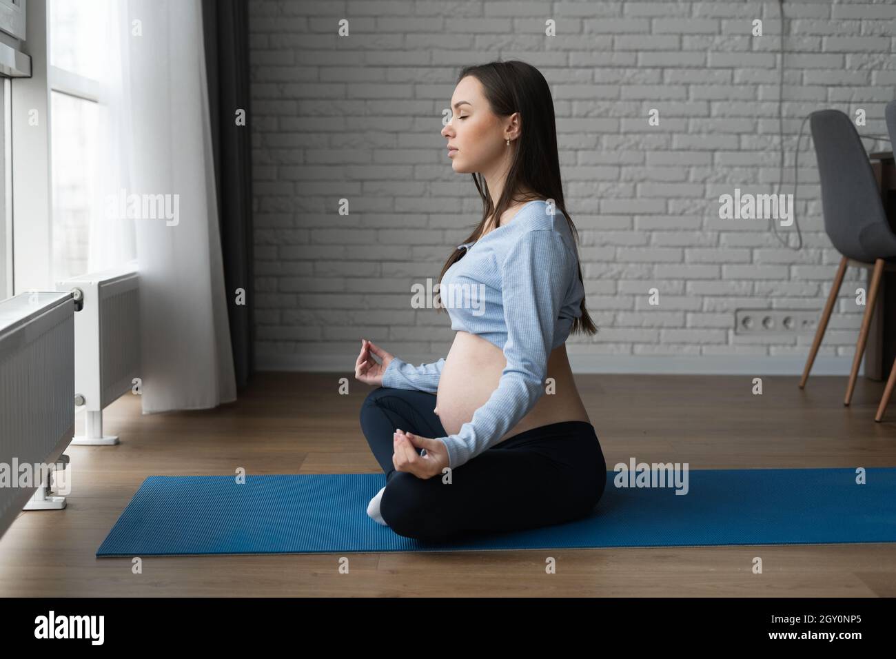 Bella donna incinta che si esercita a casa, orizzontale. Siede nella posizione del loto e medita. Foto Stock