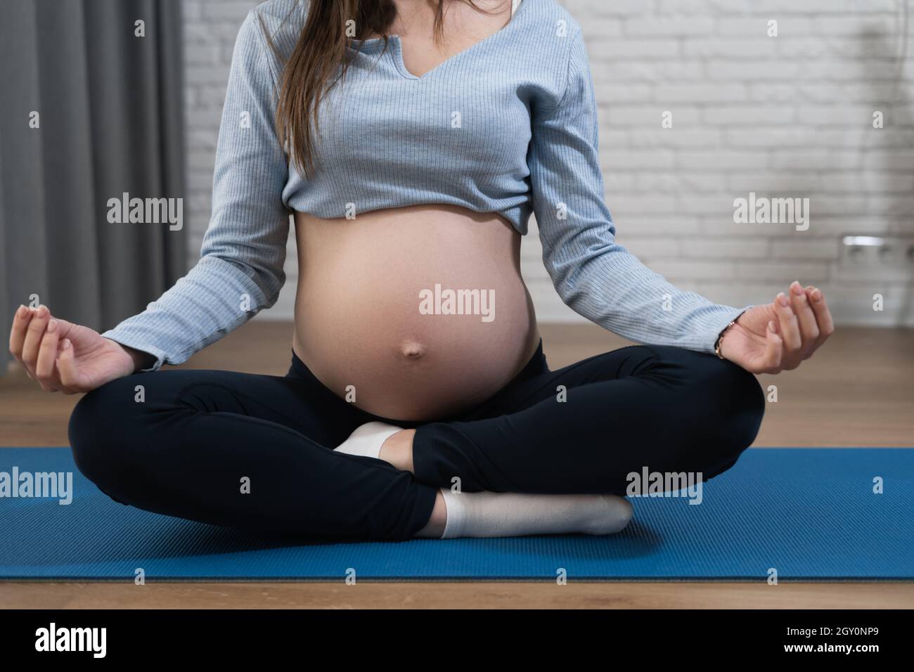 ventre di una donna incinta, si siede sul pavimento nella posizione del loto. Meditazione per le donne in attesa. Foto Stock