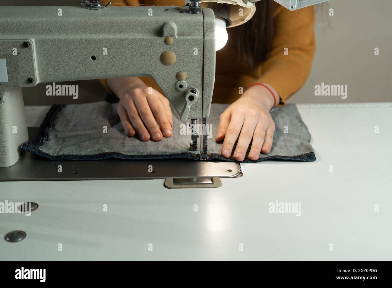 Una giovane ragazza è seduta in una macchina da cucire in officina. Cucire abiti secondo il modello dell'autore. Cucire atelier concetto. Foto Stock