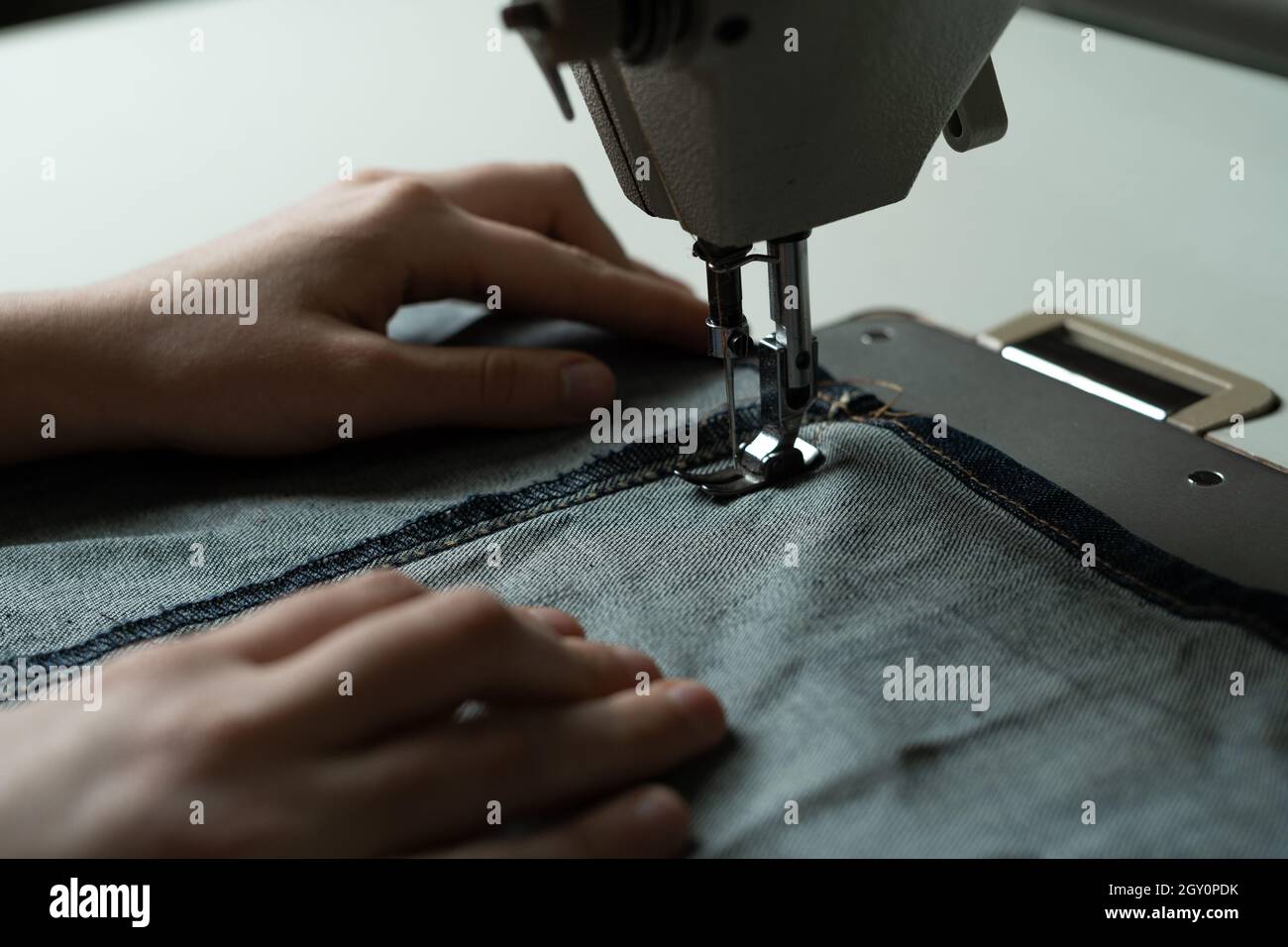 Le mani della ragazza alla macchina da cucire in officina. Biancheria da cucire secondo lo schema dell'autore. Cucire atelier concetto. Foto Stock