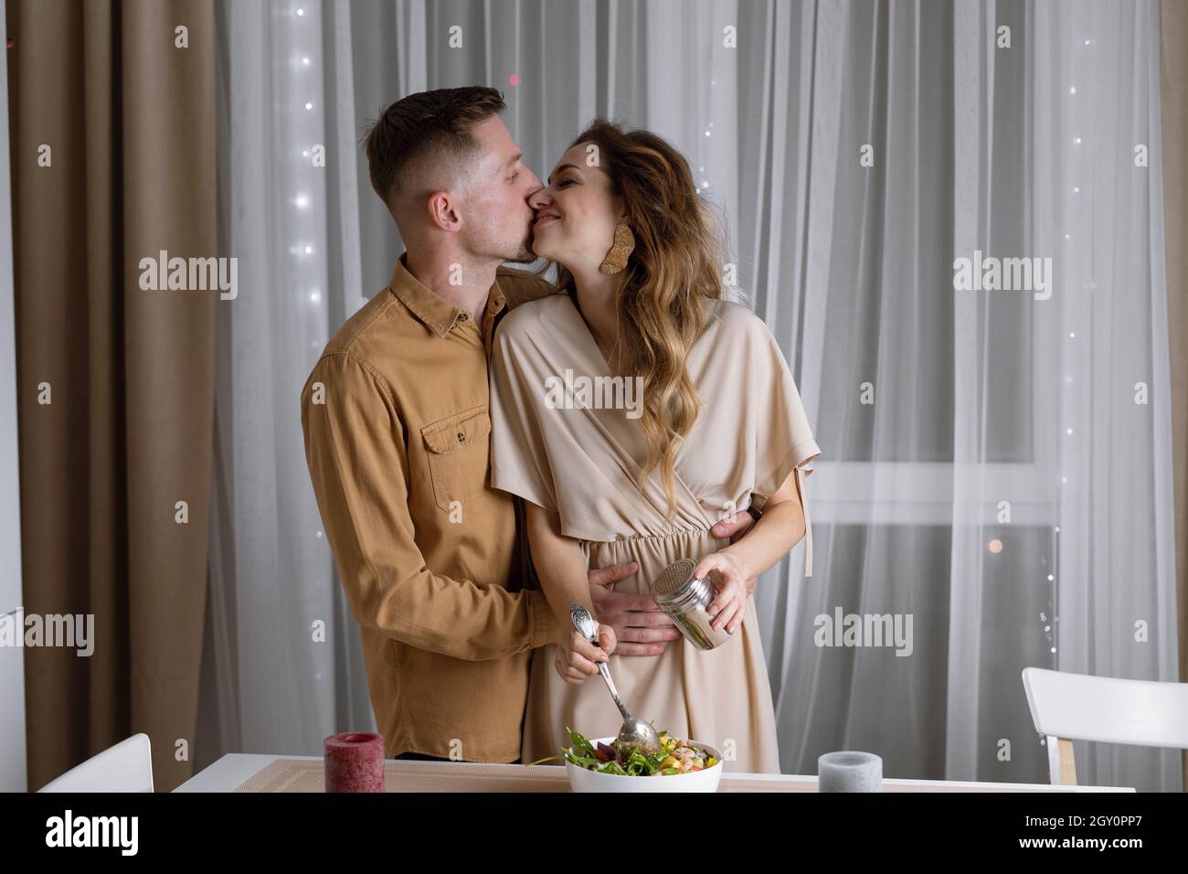 Una giovane coppia sta facendo una cena romantica insieme a casa - un uomo e una donna baciano appassionatamente vicino al tavolo. Foto Stock