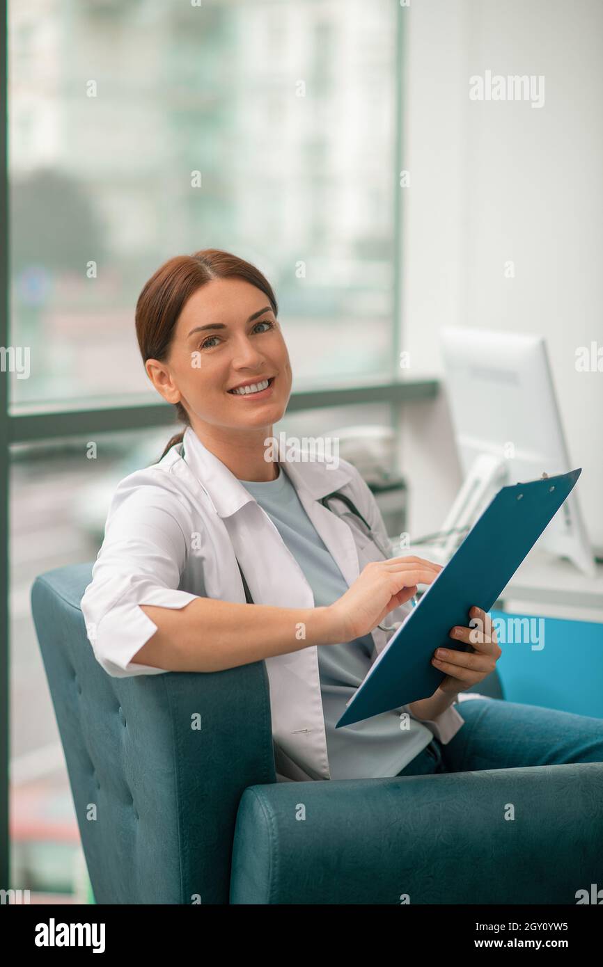 Una donna sorridente in un accappatoio bianco che tiene una lista di prescrizioni e che guarda contented Foto Stock