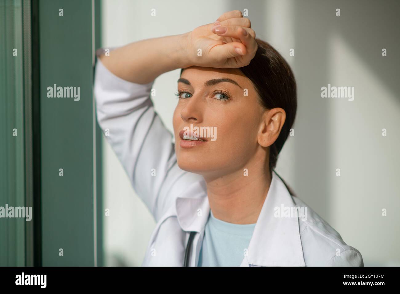 Un medico dai capelli scuri che si trova vicino alla finestra e che appare premuroso Foto Stock