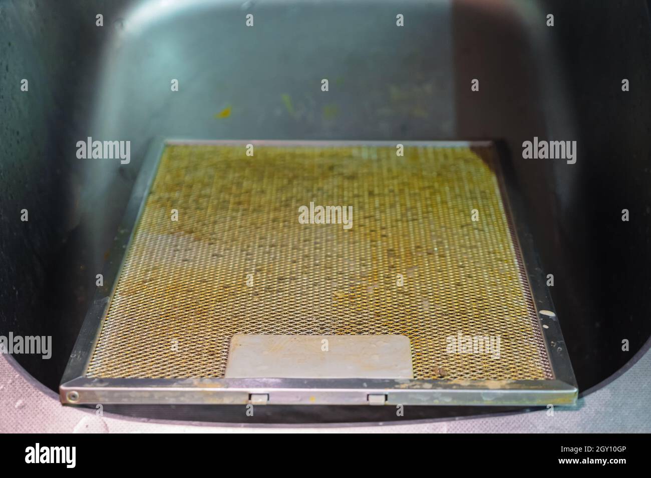 Un filtro a rete in alluminio sporco dal cofano di casa si trova nel lavandino. Il filtro del cofano è coperto di grasso Foto Stock