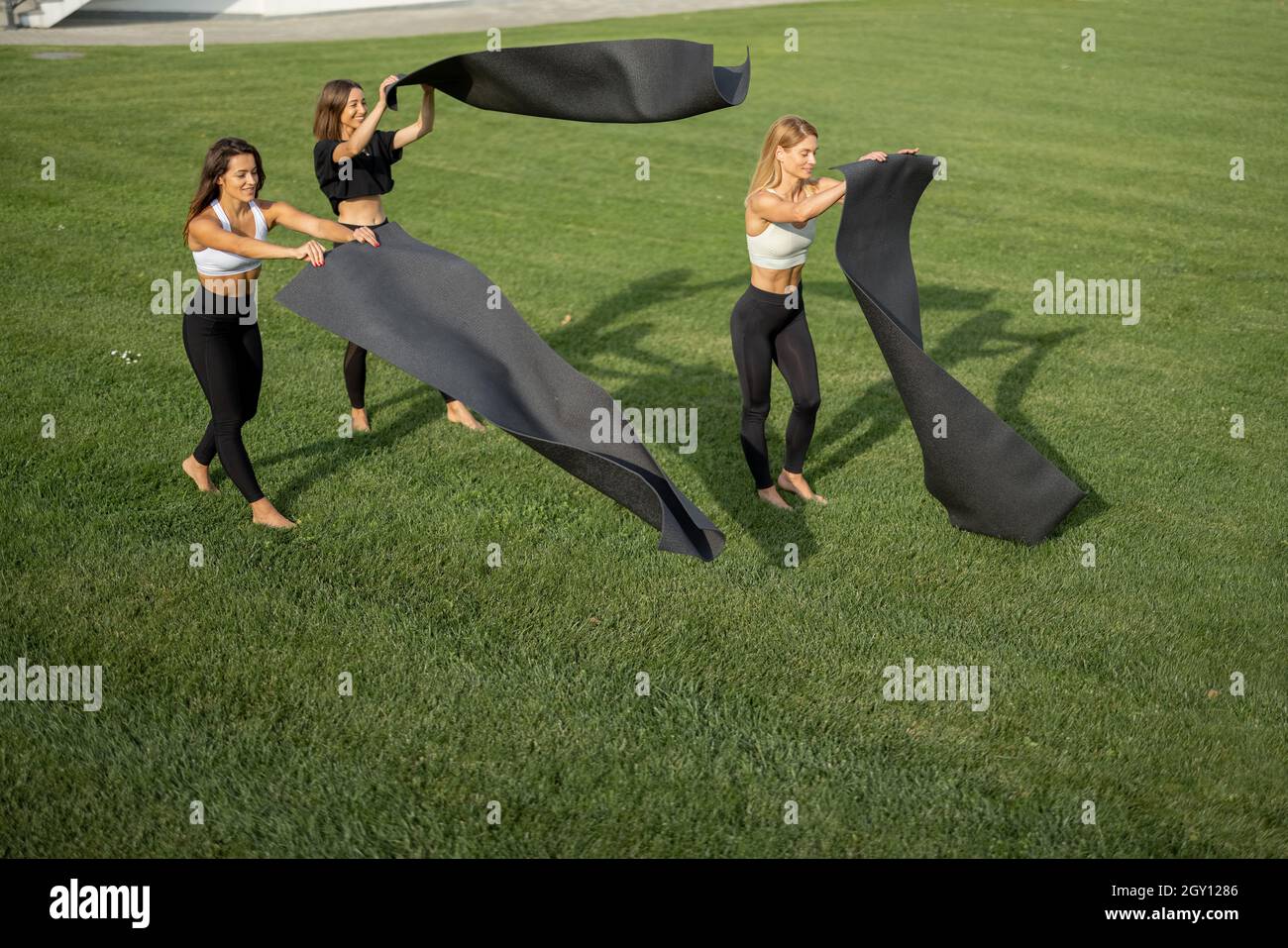 Girlfriends mettere i tappetini fitness sul prato verde Foto Stock