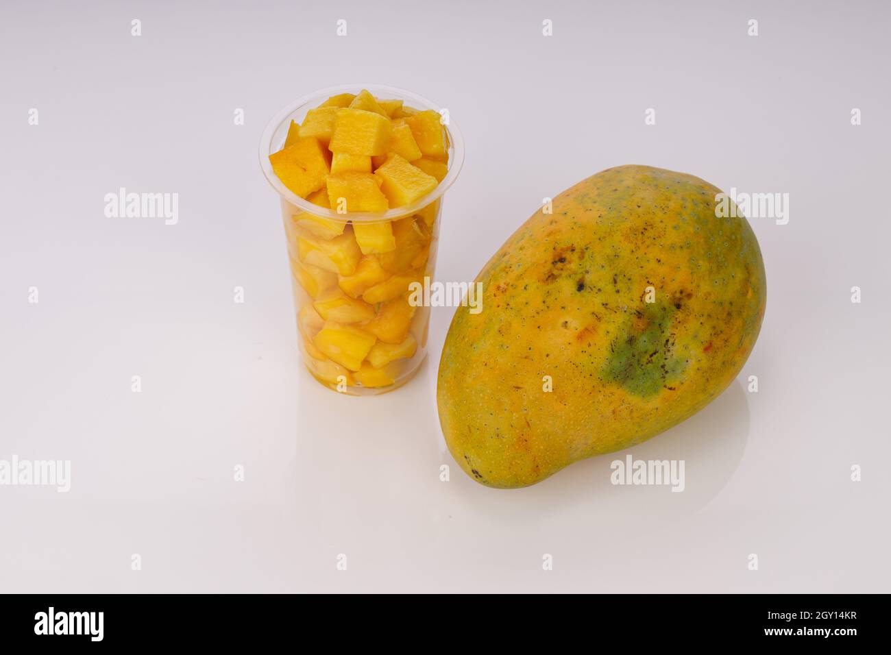 Cubi di mango maturi o pezzi tagliati disposti in vetro trasparente con mango posto vicino su sfondo bianco. Foto Stock