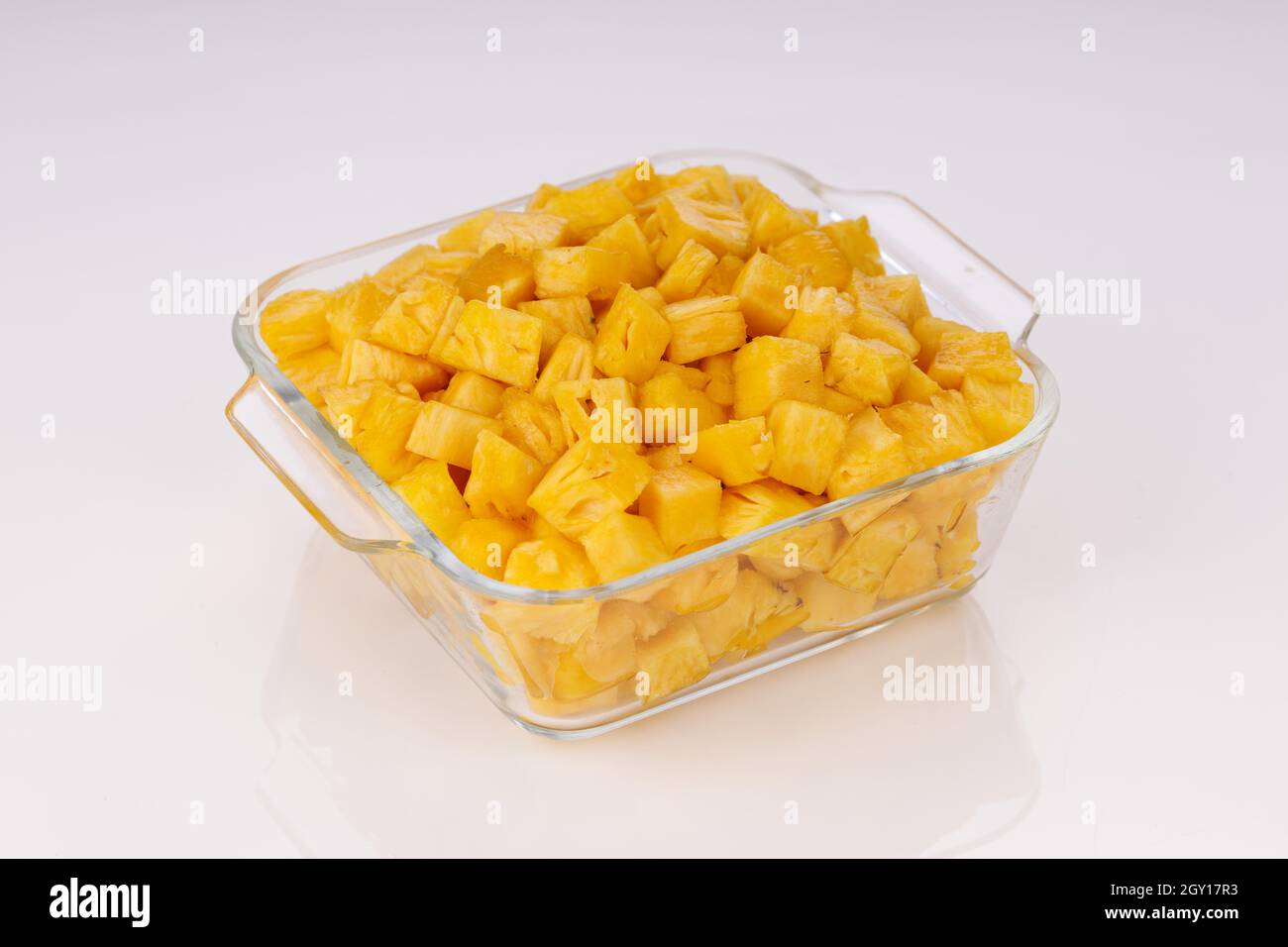 Cubetti di ananas disposti in contenitore quadrato trasparente di vetro con fondo bianco Foto Stock
