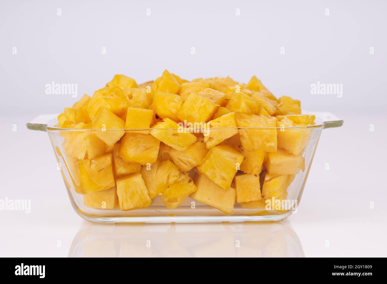 Cubetti di ananas disposti in contenitore quadrato trasparente di vetro con fondo bianco Foto Stock