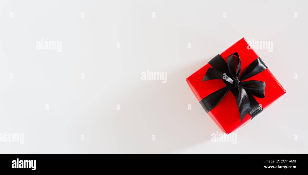 Confezione regalo in nero e rosso. Vista dall'alto di un regalo luminoso con un nastro in raso nero su sfondo bianco. Design concettuale minimalista per Bir Foto Stock