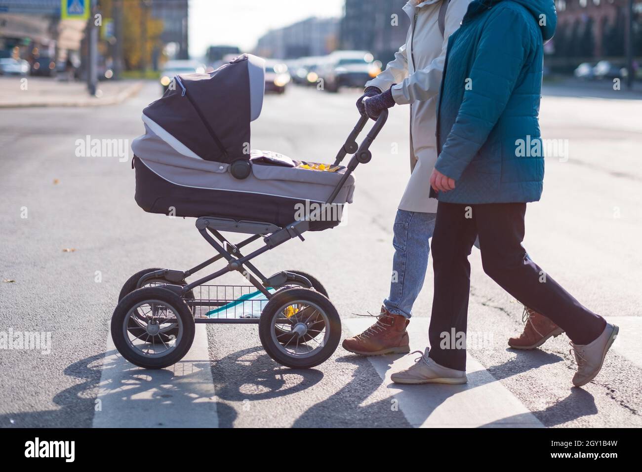 Gambe di due donne con passeggino su crosswalk attraversando la strada Foto Stock