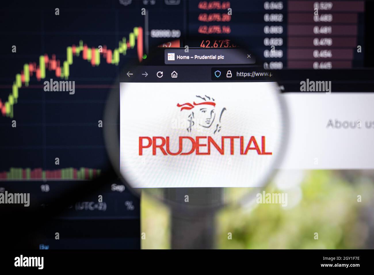 Prudential Company logo su un sito web con sviluppi sfocati del mercato azionario in background, visto su uno schermo del computer attraverso una lente di ingrandimento Foto Stock