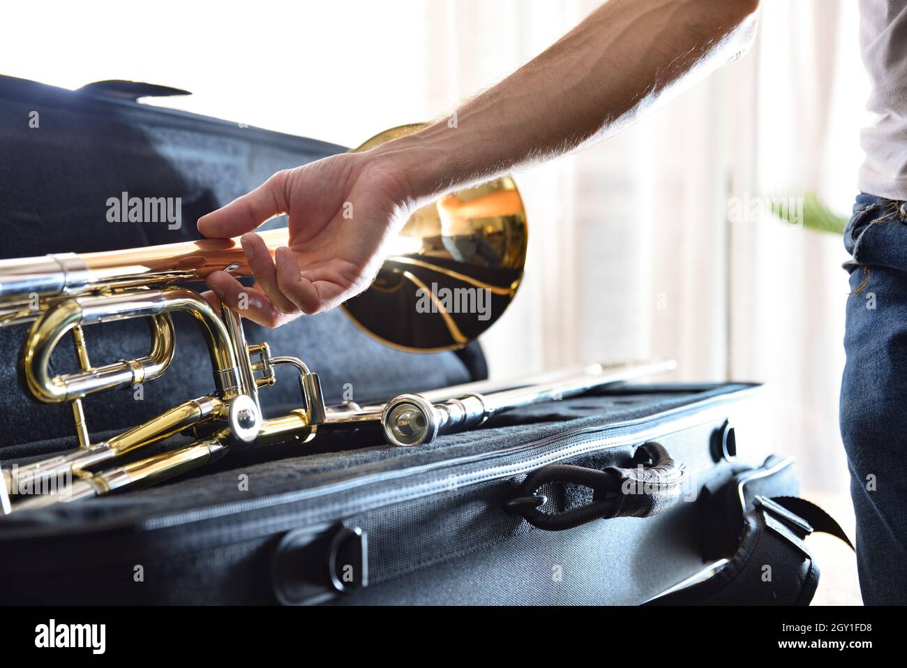 Il musicista raccoglie il trombone montato su una valigia protettiva in una stanza. Vista frontale. Composizione orizzontale. Foto Stock