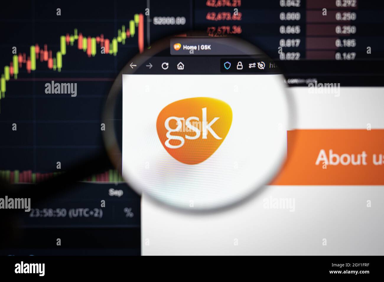 logo della gsk company su un sito web con sviluppi del mercato azionario sfocati in background, visto su uno schermo del computer attraverso una lente d'ingrandimento Foto Stock