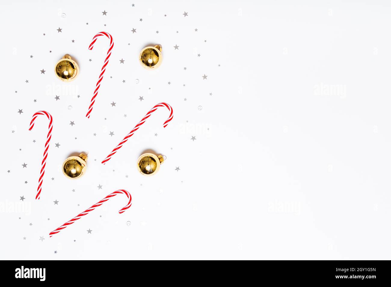 Composizione del piatto di Natale. Caramelle natalizie, palle d'oro, stelle con glitter a sfondo bianco. Design piatto, vista dall'alto, spazio di copia Foto Stock