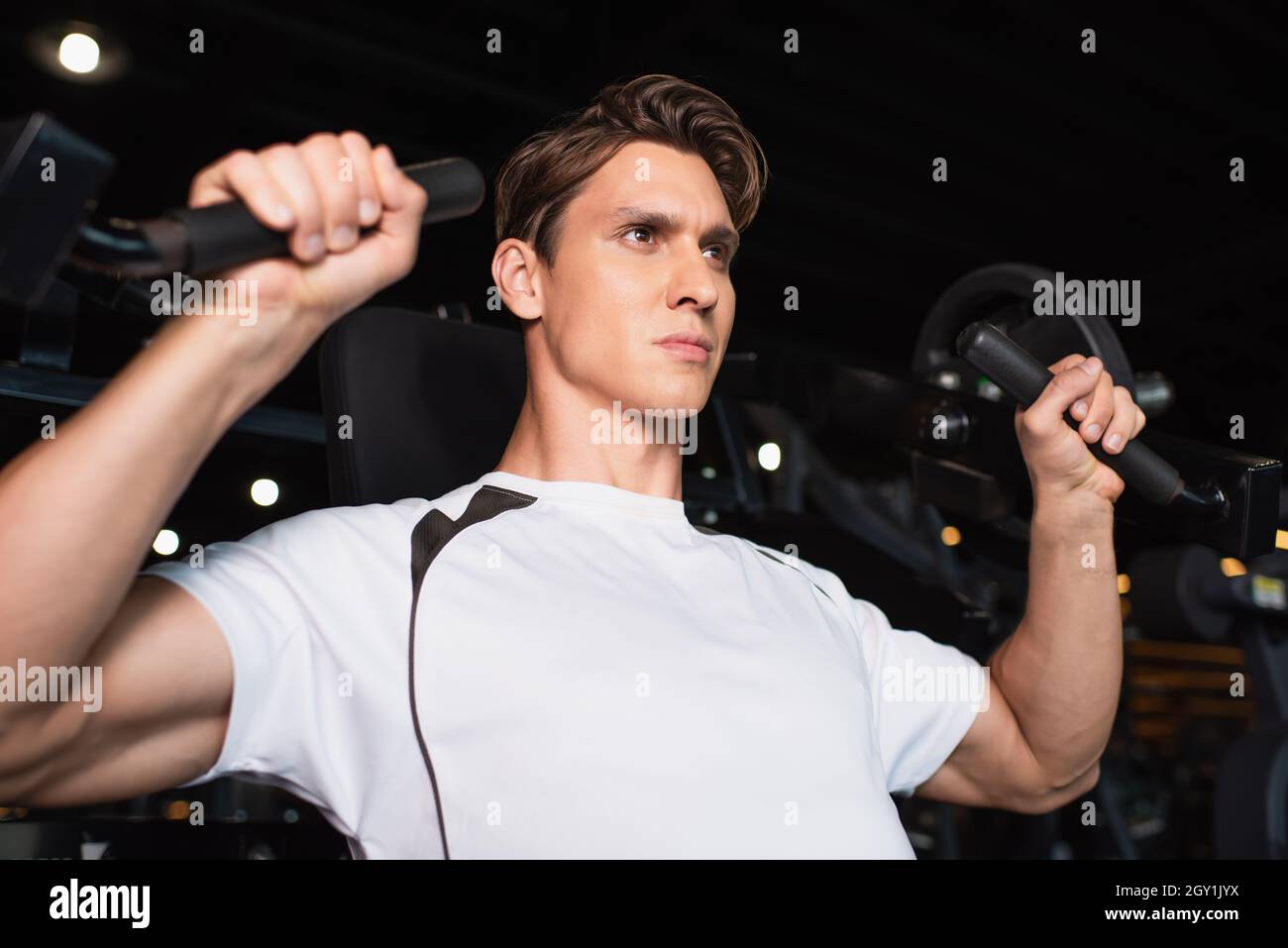 uomo sportivo che guarda via mentre si lavora sulla prolunga del braccio della macchina per esercizi Foto Stock