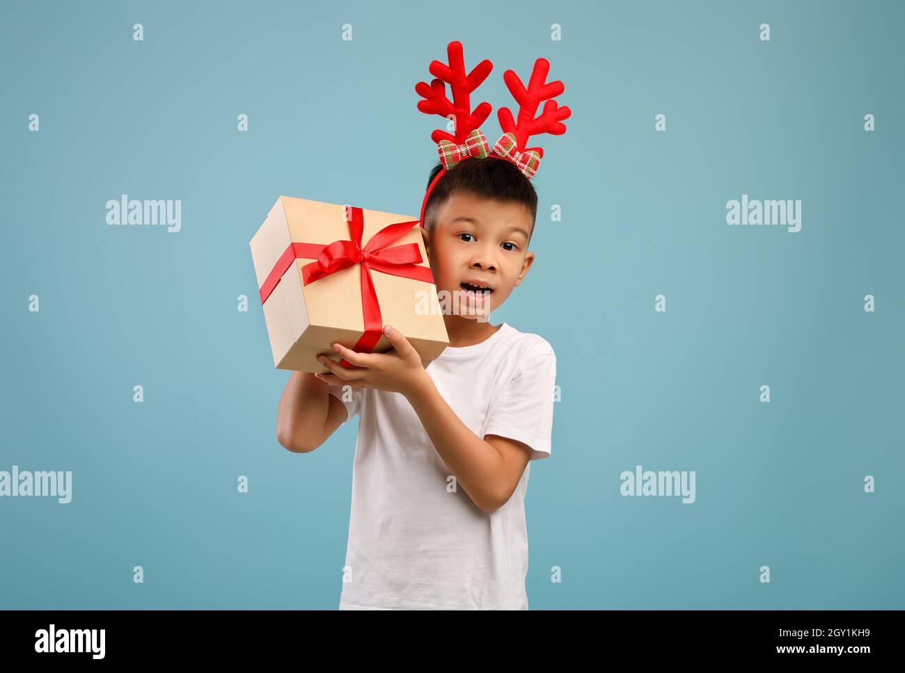 Boy Asiatico eccitato piccolo che indossa i corni di cervo di Natale che tiene la scatola presente Foto Stock