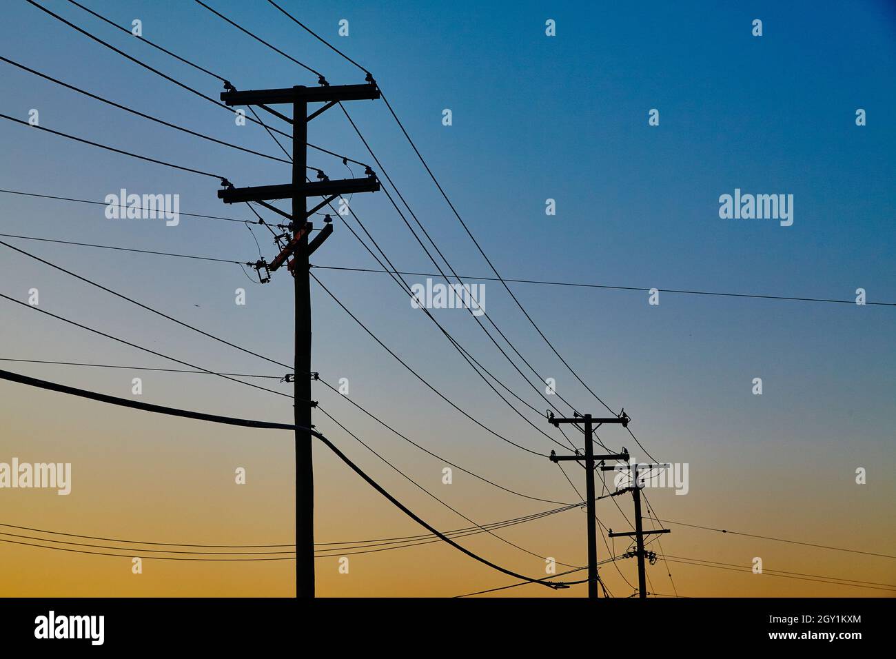 Le linee elettriche si estendono in lontananza, come il sole arancione che tramonta Foto Stock