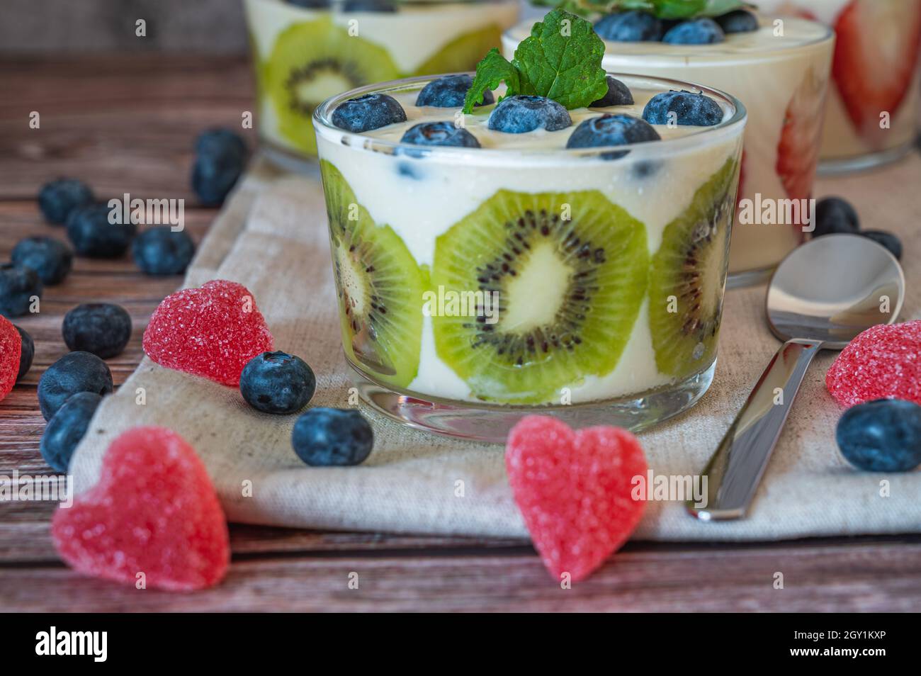 Una sana colazione fatta in casa in un bicchiere con frutta fresca: kiwi, fragola e yogurt su sfondo di legno. Profondità di campo bassa con foc selettivo Foto Stock