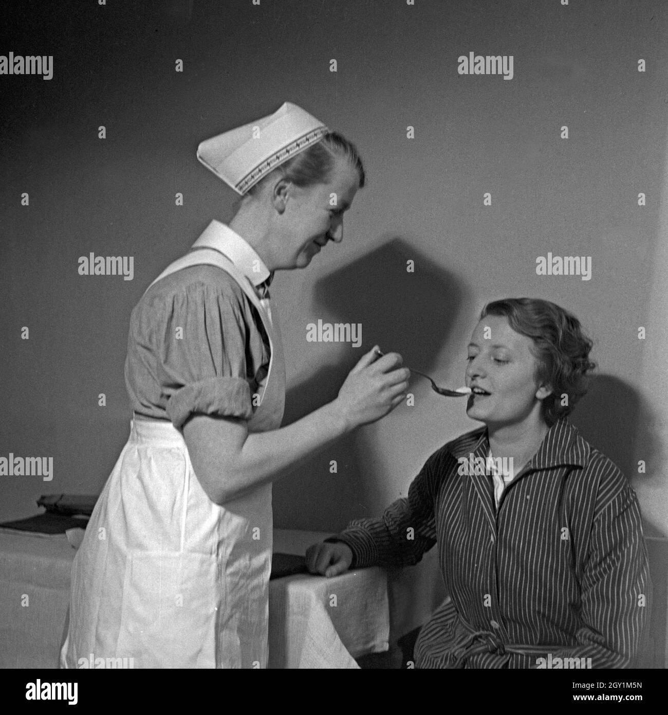 Eine Schwester des Deutschen Roten Kreuzes verarbreicht einer Kranken einen Löffel Medizin, Deutschland 1930er Jahre. Un nburse della Croce Rossa tedesca applicando alcune medicine per una donna malata, Germania 1930s. Foto Stock