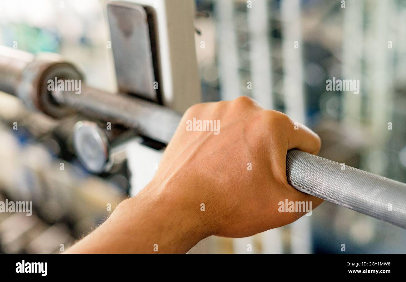 Mano dell'uomo che afferra un barbell in palestra. Fitness, esercizio fisico, sollevamento pesi e motivazione palestra. Concetto di stile di vita sano. Profondità di campo poco profonda. Foto Stock