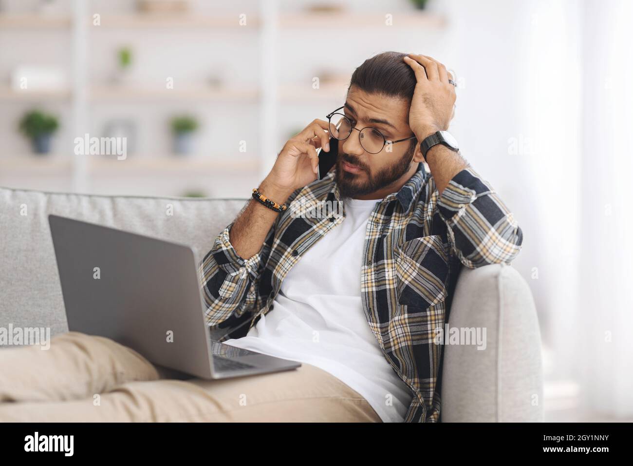 Stressante ragazzo indiano con un computer portatile che ha una conversazione telefonica Foto Stock