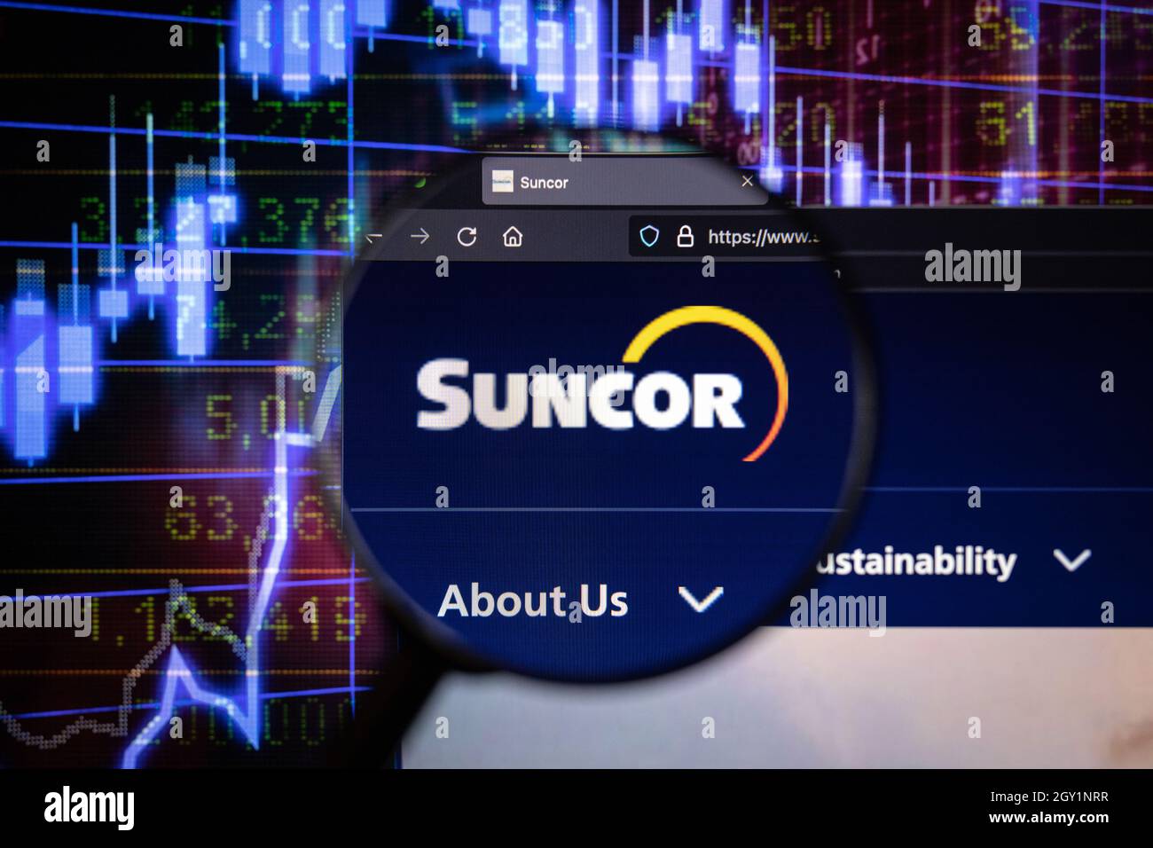 Suncor Company logo su un sito web con blurry mercato azionario sviluppi in background, visto su uno schermo di computer attraverso una lente d'ingrandimento Foto Stock