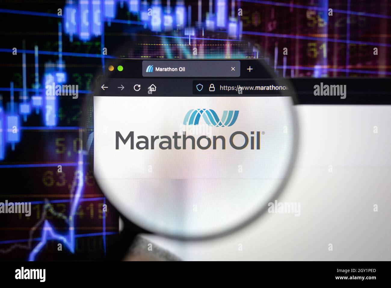 Marathon Oil logo di un'azienda su un sito web con sviluppi sfocati del mercato azionario in background, visto su uno schermo del computer attraverso una lente di ingrandimento Foto Stock