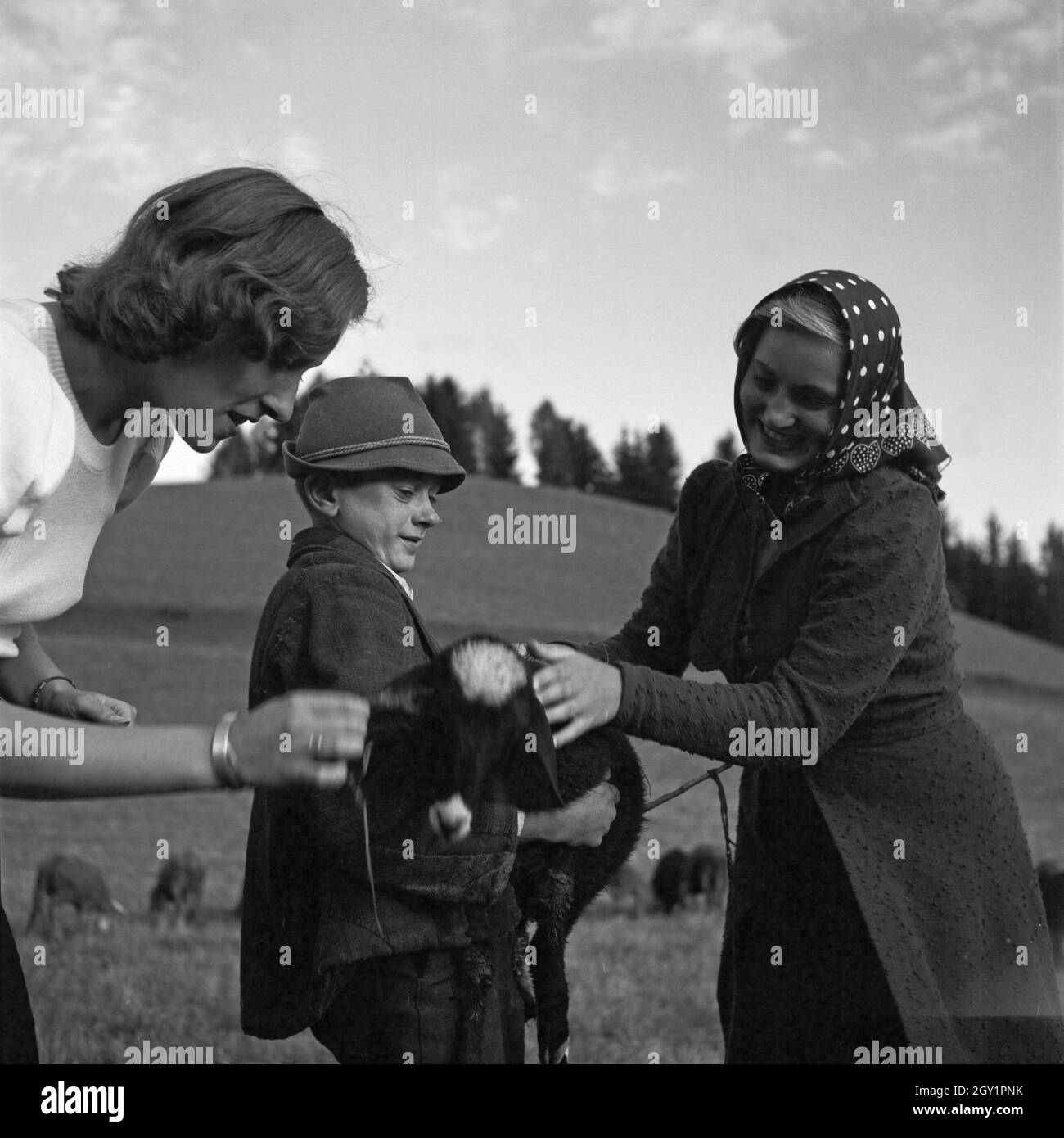 Zwei junge Frauen und ein Hirtenjunge spielen auf einer Alm Mit einem Lamm, Deutschland 1930er Jahre. Due giovani donne e un pastore giocando con un po' di agnello su un prato, Germania 1930s. Foto Stock