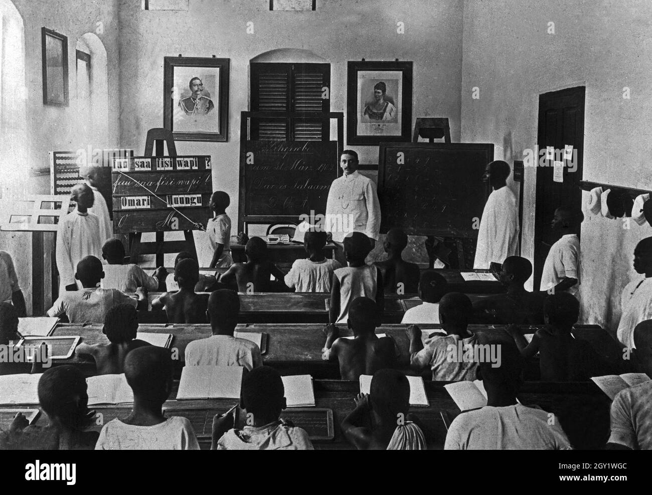 Unter dem Strengen Blick von Kaiser Wilhelm und Seiner Frau Auguste Viktoria lernen die afrikanischen Schulkinder lesen, Deutsch-Ostafrika 1900er Jahre. I ragazzi africani imparano a scrivere e leggere, il 1900 dell'Africa orientale tedesca. Foto Stock