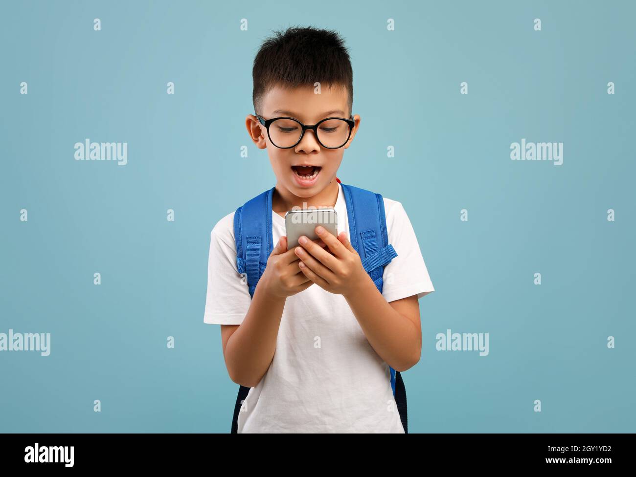 Ragazzo asiatico entusiasta con zaino con smartphone su sfondo blu Foto Stock