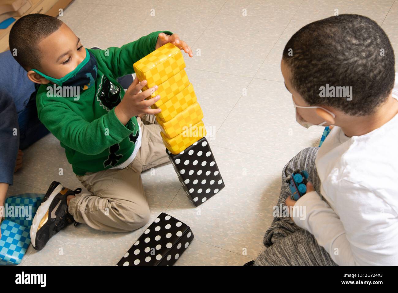 Istruzione Preschool 3-4 anni due ragazzi in blocco area giocare con blocchi colorati in schiuma blocchi, un ragazzo impilamento, mentre gli altri orologi, entrambi indossando fac Foto Stock