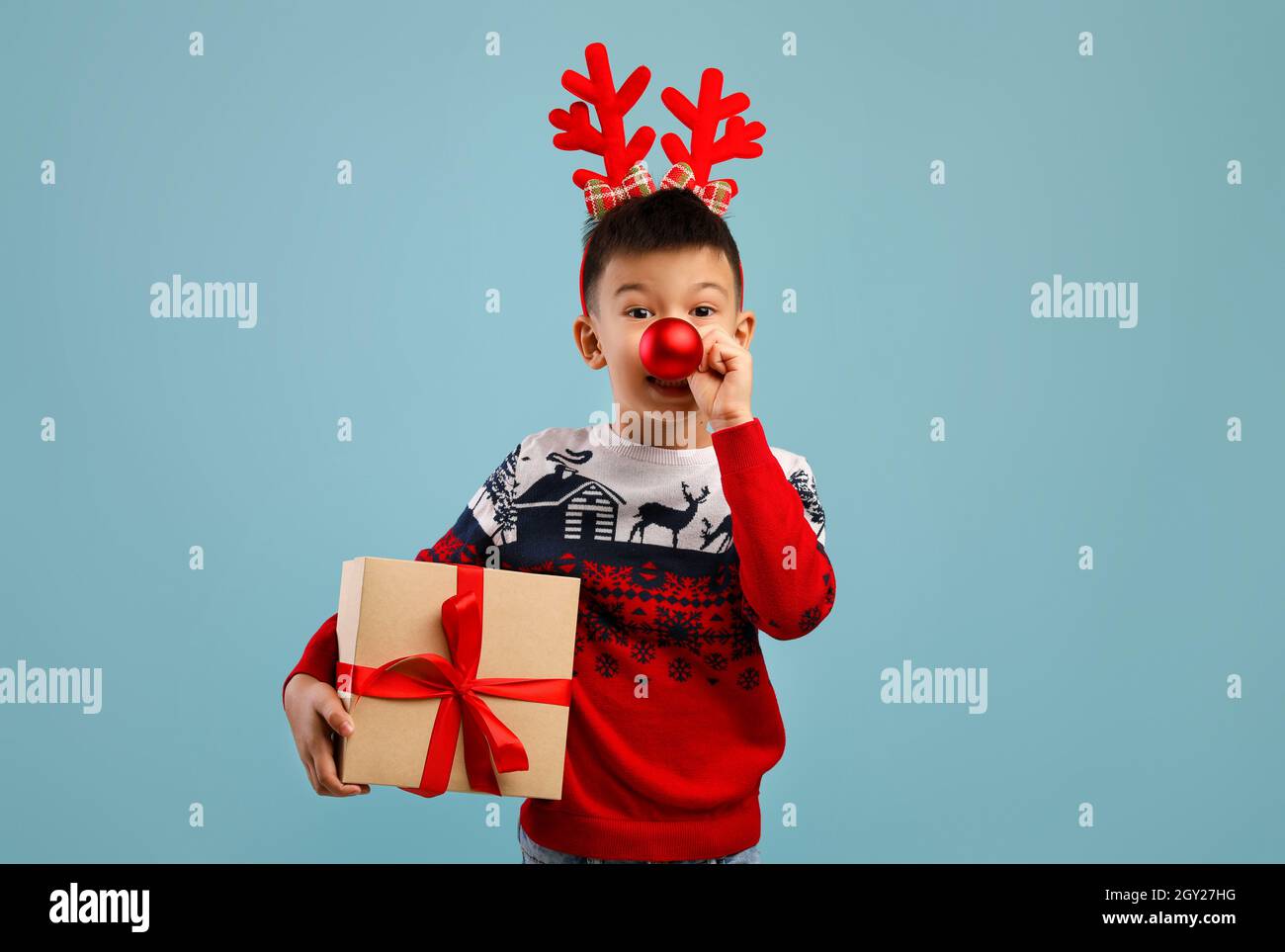 Divertimento per le vacanze. Asian Boy che indossa Coro del cervo e Christmas Sweater Holding presente Foto Stock