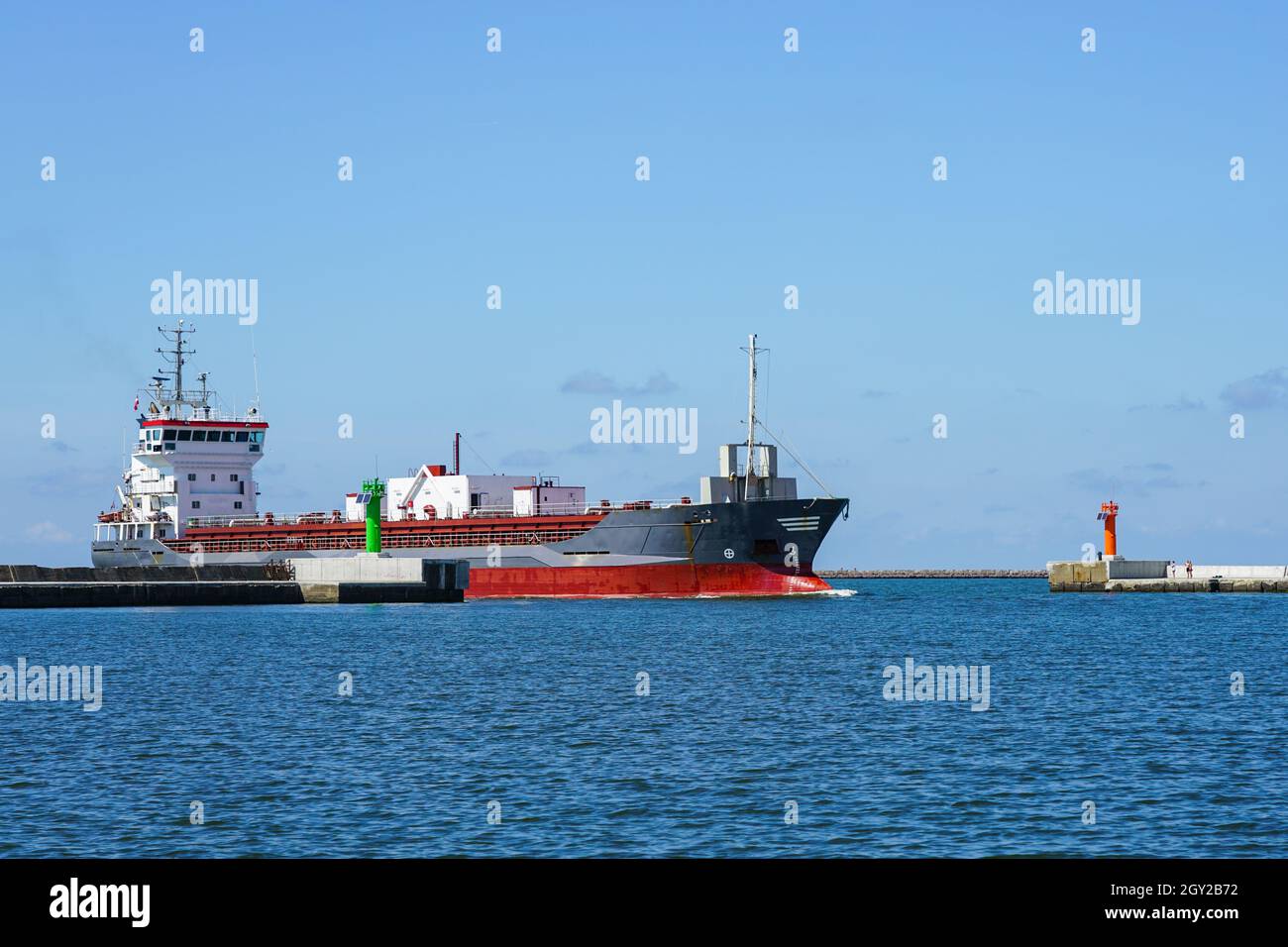 un'imbarcazione per il trasporto di cemento entra nel porto attraverso cancelli di frangiflutti dotati di torri di segnalazione di navigazione Foto Stock
