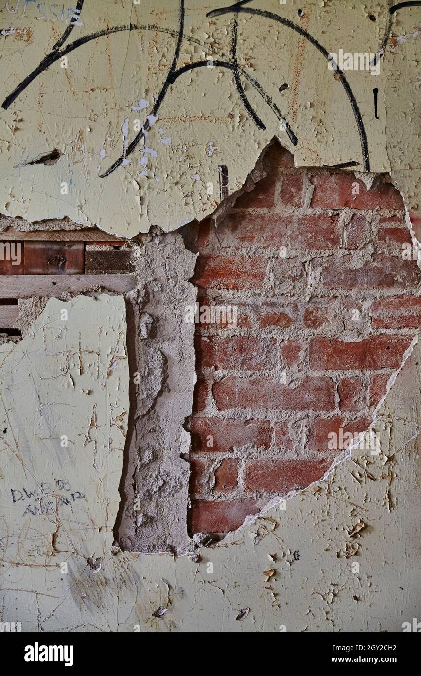 Vecchia parete di cemento dilapidata che si stacca via per rivelare mattoni con sfondo nero graffiti Foto Stock