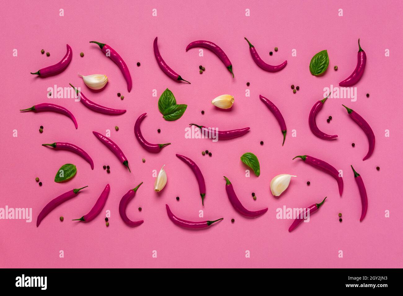 Immagine rosa di peperoncini caldi crudi, foglie di basilico verde fresco, pochi spicchi d'aglio e grani di pepe nero su sfondo di rosa lilla. Gelato alle spezie Foto Stock